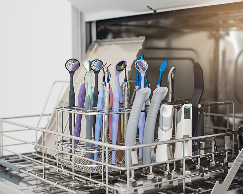 The image shows a dishwasher with various toothbrushes placed inside its basket, suggesting an unusual use of the appliance for cleaning the brushes rather than dishes.