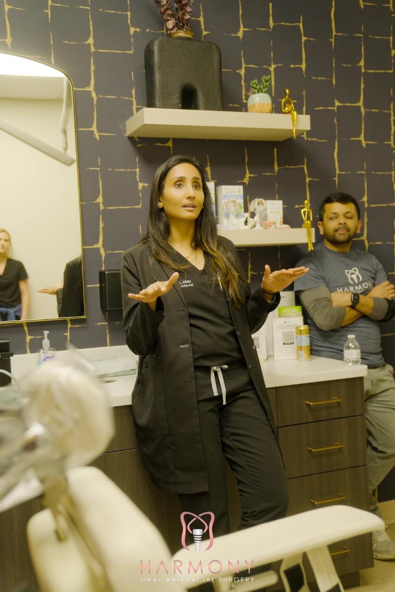 Woman in scrubs gesturing with hands while standing in front of dental chair.