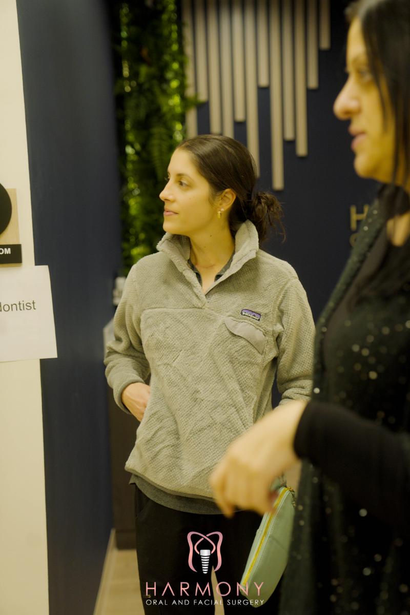 The image shows two individuals inside an office environment, with one person standing and looking at a sign on the wall while another person stands beside them, both appearing to be engaged in a conversation or observing something together.