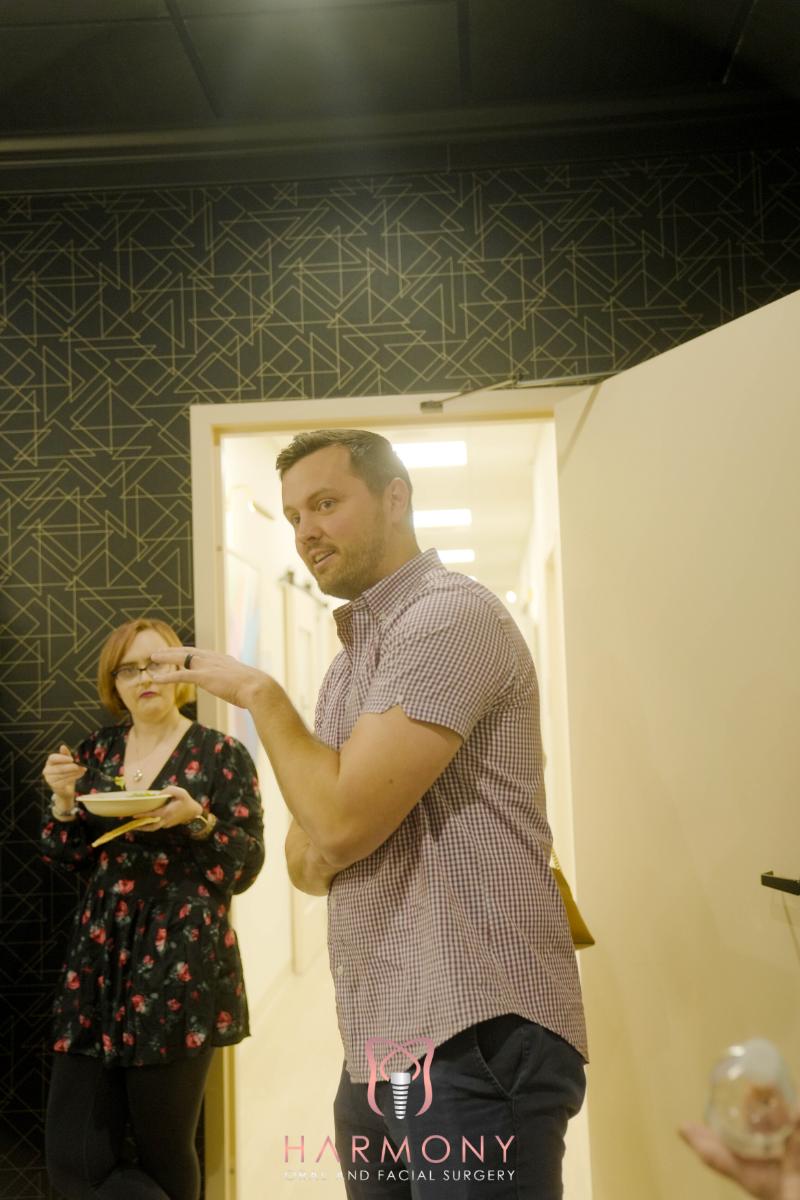 A man standing next to a woman in an indoor setting, both appearing to be engaged in a social event with food and drinks.