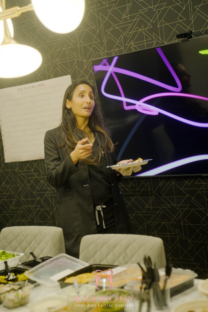 A woman stands at a table with food, gesturing towards something out of frame.
