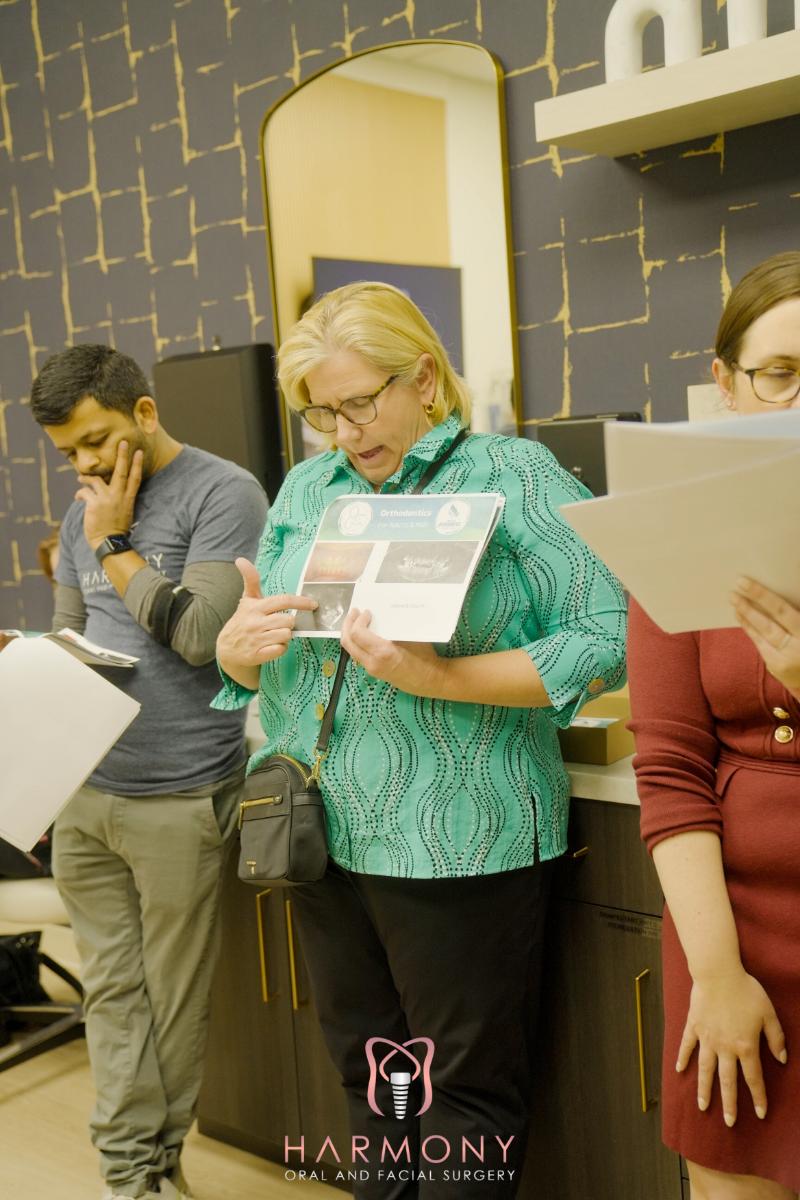 Woman holding a pamphlet at a table with others, likely in an educational or informational setting.