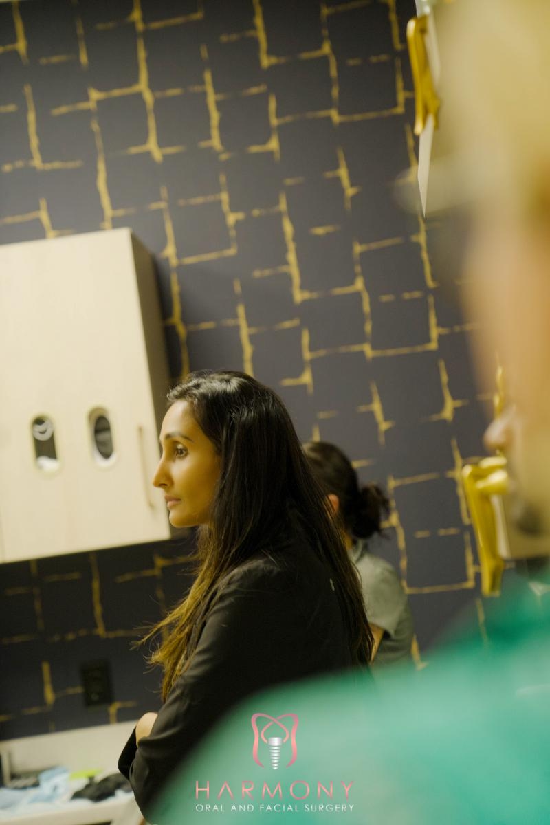 A woman stands in front of a counter with a patterned backdrop, looking slightly to her right.