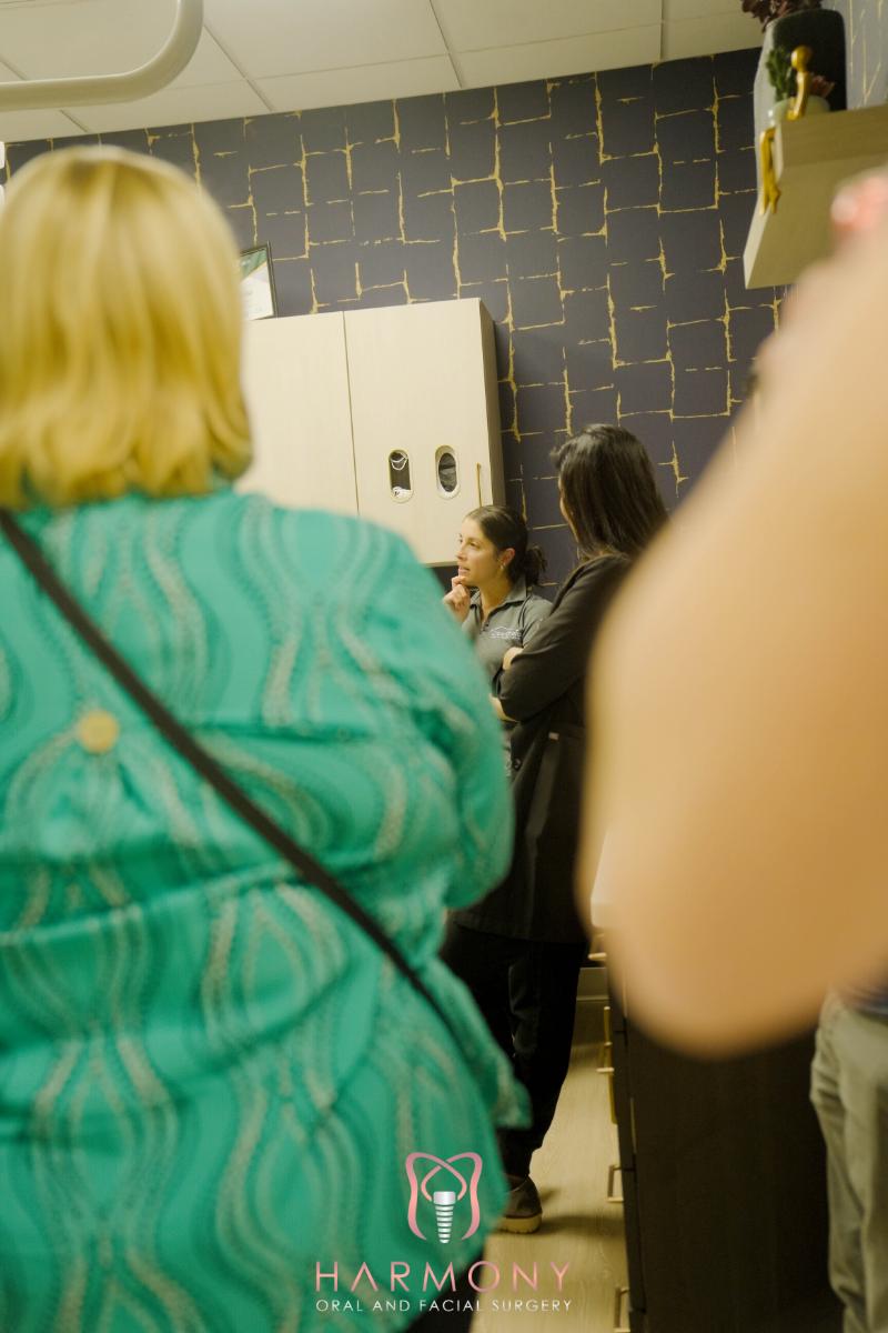 The image shows an indoor setting where people are gathered around, with a person standing at a counter and others conversing.