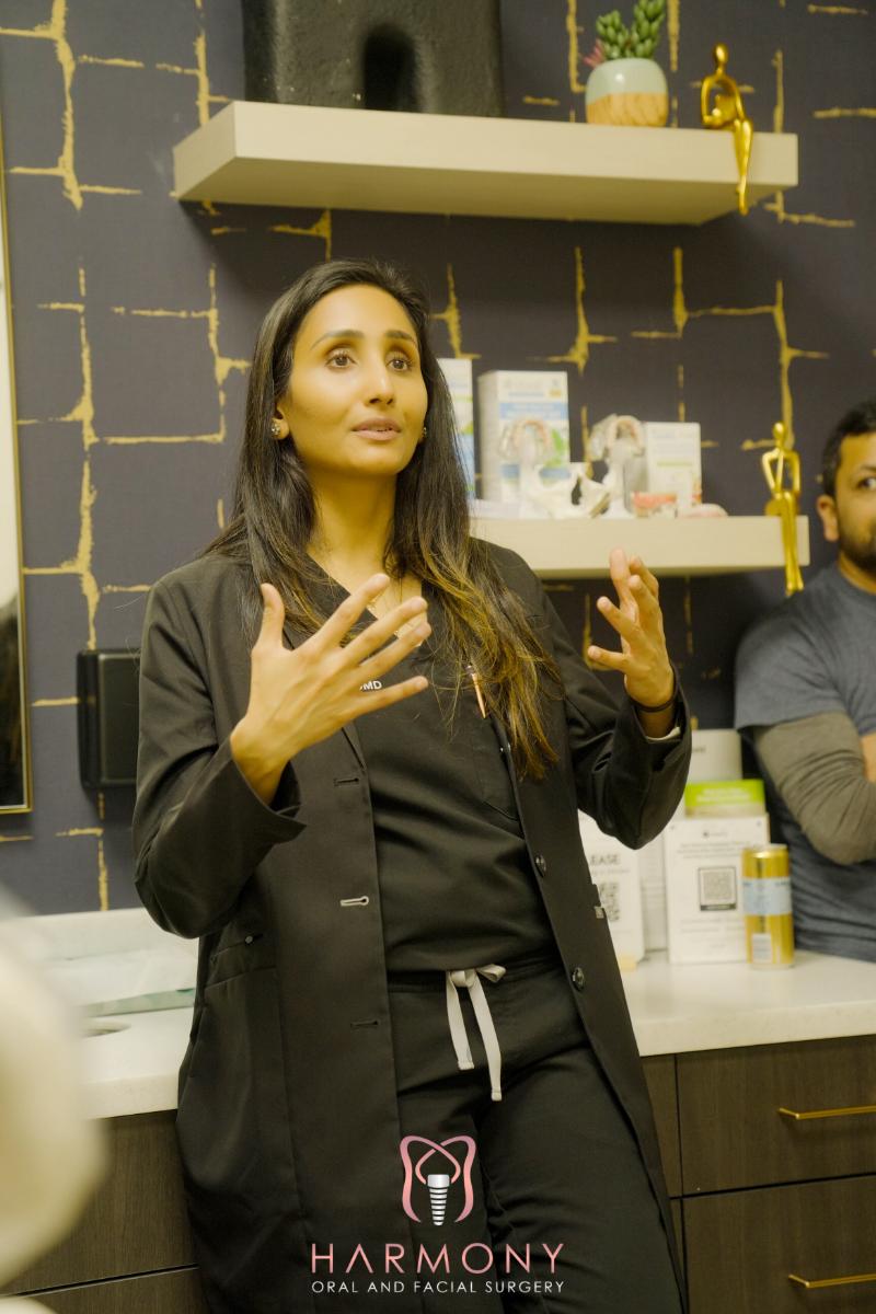 A woman, possibly a medical professional, gesturing with her hands while standing indoors, likely in a store or office setting, surrounded by shelves of products.