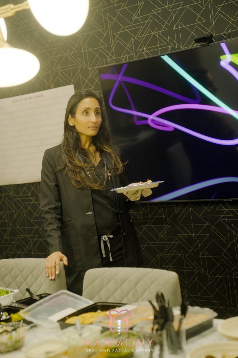 A woman standing in front of a presentation screen, holding a plate with food on it, in an office setting.