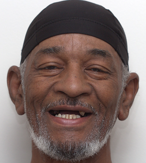 The image shows a man with a beard and mustache wearing a black headband and smiling at the camera.